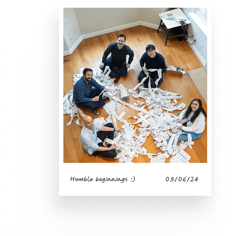 Polaroid captioned Humble beginnings 09/06/24, five people sitting on the floor amid long paper receipts